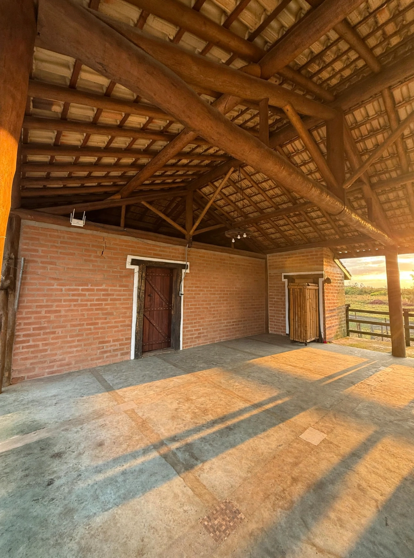 Interior do salão mostrando a estrutura de vigas cruzadas do telhado e portas de madeira e bambu